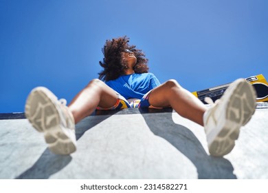 Low angle view carefree young woman with boom box sitting at edge of sports ramp below sunny blue sky - Powered by Shutterstock