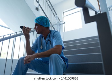 Low angle view of Caucasian male surgeon talking on mobile phone in speaker on the stairs of hospital - Powered by Shutterstock
