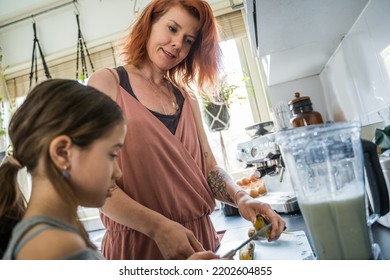 Low angle view of the caucasian mother standing at the kitchen and helping her daughter cooking smoothie for the breakfast. Stock photo 