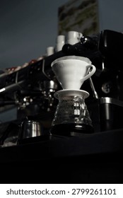 Low angle view of ceramic V60 dripper with paper filter placed on glass coffee server in specialty coffee shop atmosphere.