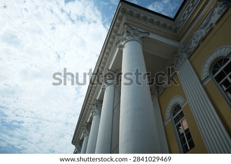 Low angle view of classical building with ornate Corinthian columns, decorative entablature, carved cornice details and yellow facade beneath cloudy sky, with column, corinthian, capital