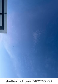 A low angle view of a clear blue sky with a small portion of a modern building corner visible on the left side.
