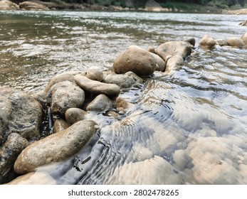 Low angle view of clear river water creating ripples over rocks and stones in a flowing stream