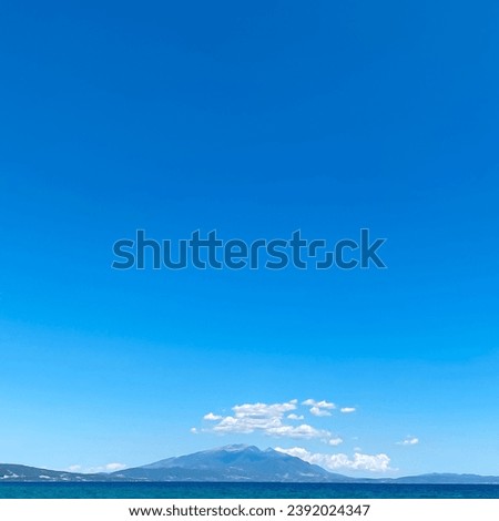 Low angle view of clear sea water with mountains in the distance under a blue sky with clouds.