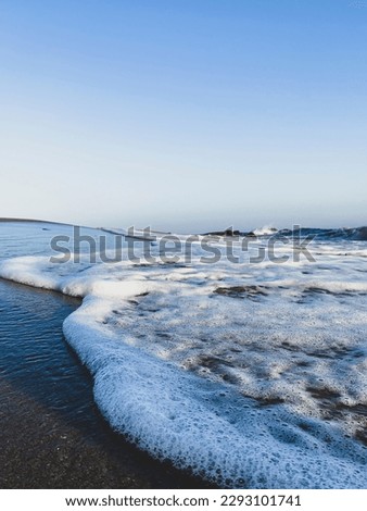 Low angle view close up of gentle surf with wave and foam on a sandy beach against blue sky