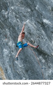 LOW ANGLE VIEW, CLOSE UP: Agile male climber moves up a challenging rock face. Focused young man shows incredible power and determination while overcoming a difficult section on a French climbing site