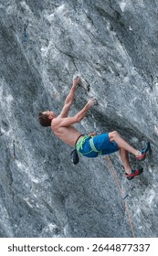 LOW ANGLE VIEW, CLOSE UP: Athletic young man climbs an overhanging rocky cliff in the Alps. Focused and experienced lead climber prepares for the next move in overcoming a difficult climbing route.