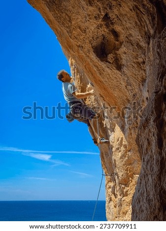 LOW ANGLE VIEW, CLOSE UP: Sport climber on an overhanging limestone route with the Mediterranean Sea on the horizon. Male athlete climbing against bright blue sky and sunlit rock in western Sicily.