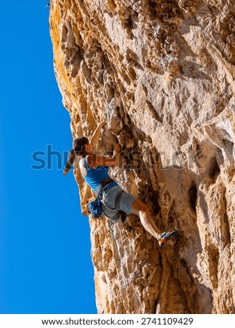 LOW ANGLE VIEW, CLOSE UP: Woman lead climbing steep limestone tufas on an overhang in western Sicily. Her body position shows strength and balance as she deals with challenging route under blue sky.