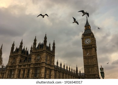 Low angle view of cloudy and dark sky above Westminster Palace and Big Ben clock tower with birds flying in sky. 