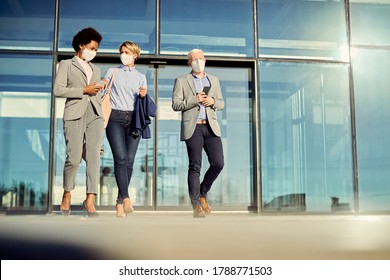 Low angle view of colleagues wearing protective face masks while leaving office building and communicating. Copy space.  - Powered by Shutterstock