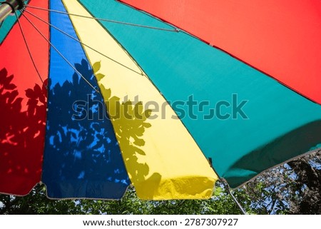 Low angle view of a colorful multi colored parasol with tree leaf shadows on a sunny day.