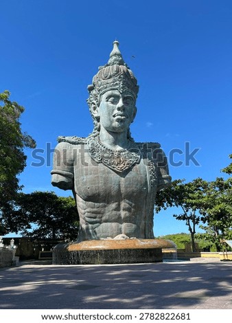Low angle view of a colossal Hindu deity statue torso against a clear blue sky.