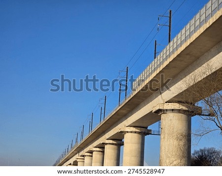 Low angle view of a concrete elevated train track with electric power lines and blue sky background.