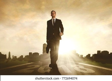 Low angle view of confident businessman holding a briefcase while walking above number 2018 in the road with skyscraper background - Shutterstock ID 772694074