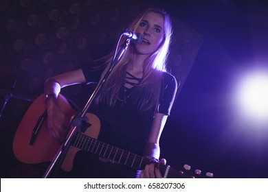 Low angle view of confident female singer performing with guitar in nightclub