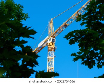 low angle view of a construction tower crane through green foliage. Funds for building construction