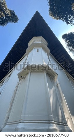 A low angle view of the corner of a historic white building featuring a dark wooden roof against a bright blue sky.