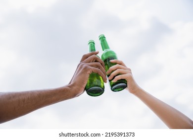 low angle view of cropped interracial friends clinking beer bottles - Powered by Shutterstock