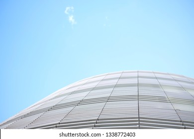 Low angle view of a curved facade detail of a small modern office building, white construction against light blue sky and a white cloud.