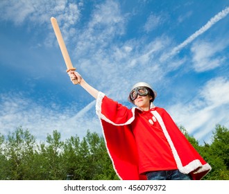Low angle view of cute teenage boy wearing metal colander as a helmet goggles and red costume holding wooden sword pretending to be a power super hero