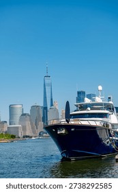 Low angle view of a dark blue yacht at a pier with One World Trade Center in the distance.
