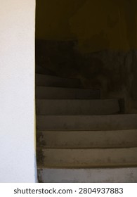 A low angle view of a dark concrete staircase leading up into a dim entryway, contrasted with a bright white external wall.