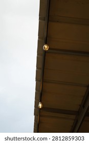 Low angle view of decorative string lights hanging from the metal roof eave against a bright sky.