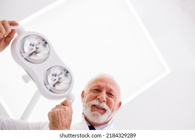 Low Angle View Of Dentist Adjusting Reflector Lights Above Patient's Head Sitting In Dental Chair