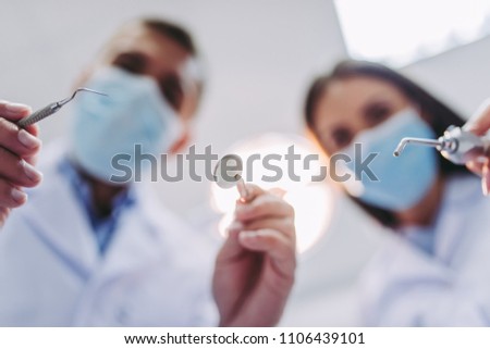 low angle view of dentist and assistant holding dental tools in modern dental clinic