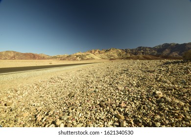 Low Angle View Desert With Road Going Through Against Mountains And Clear Blue Sky