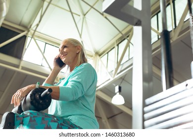 Low angle view of disabled active senior Caucasian woman with leg amputee talking mobile phone in fitness studio. Strong active senior female amputee training and working out - Powered by Shutterstock