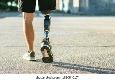 Low angle view at disabled young man with prosthetic leg walking along the street.