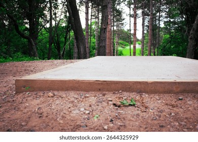 Low angle view of a disc golf concrete tee pad on a frolf course. nature landscape background. sports and recreation design element.