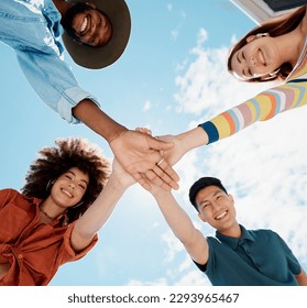 Low angle view of diverse group of people standing huddled together with hands piled in the middle. African American woman with an afro. Millennial social clique stacking hands in unity and support