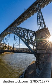 Low angle view of Dom Luis I bridge spanning the Douro river in Porto Portugal. Iconic iron structure with cityscape and waterfront, showcasing historic architecture and urban landscape.