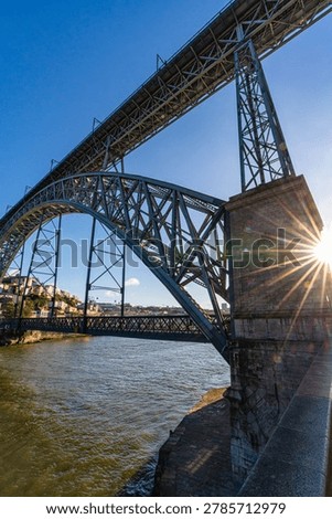 Low angle view of Dom Luis I bridge spanning the Douro river in Porto Portugal. Iconic iron structure with cityscape and waterfront, showcasing historic architecture and urban landscape.