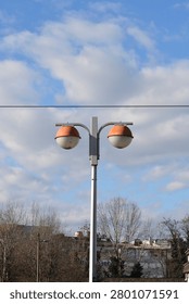 Low angle view of a double sided retro street lantern with spherical globes and orange lids under a blue sky with white clouds.