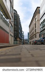 Low angle view down a quiet London street between modern office buildings with parked cars under an overcast daytime sky.