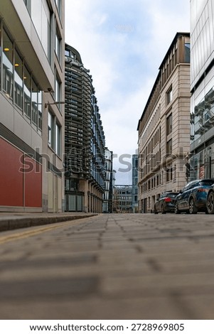 Low angle view down a quiet London street between modern office buildings with parked cars under an overcast daytime sky.