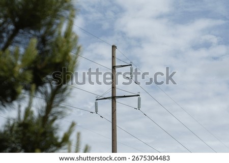 Low angle view of electrical power transmission pole with green glass insulators and crossbeams against cloudy sky. High voltage distribution infrastructure