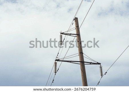 Low angle view of electrical power transmission pole with green glass insulators and crossbeams against cloudy sky. High voltage distribution infrastructure