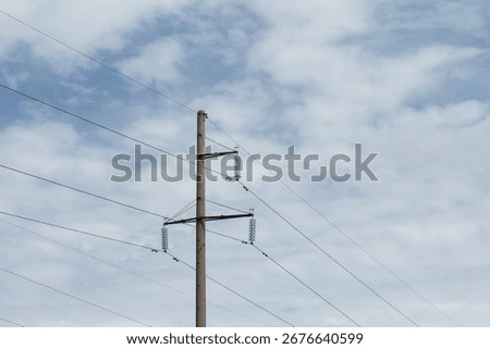 Low angle view of electrical power transmission pole with green glass insulators and crossbeams against cloudy sky. High voltage distribution infrastructure