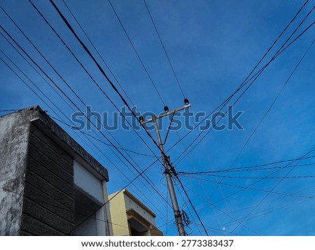 Low angle view of electricity pole with multiple power lines against a clear blue sky in Indonesia, urban infrastructure concept.