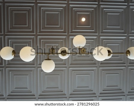Low angle view of an elegant gold sputnik pendant light fixture with frosted glass balls against a textured square panel ceiling.