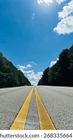 Low angle view of empty highway with yellow lines under sunny blue sky