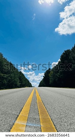 Low angle view of empty highway with yellow lines under sunny blue sky