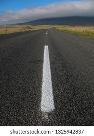 Low Angle View Of Empty Road Winding Into Distance With White Lines And Moody Clouds Over Mountains On Horizon.
