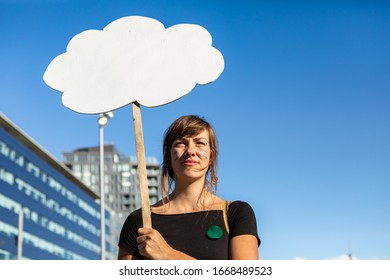 A low angle view of an environmental activist holding a thought bubble shape sign, white with copy space, with blurry city building at climate protest