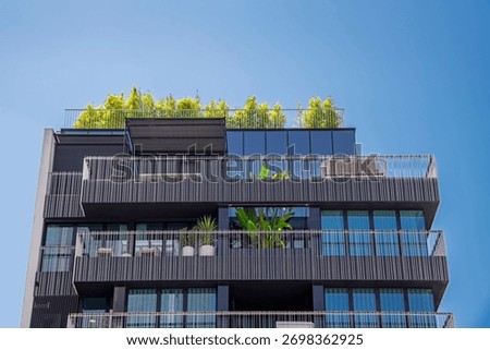 Low angle view of the facade of a modern building with green trees on the balconies and roof against a clear blue sky